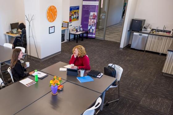 Photo of two women sitting at a conference table at Chatham Eastside, talking and drinking coffee. 